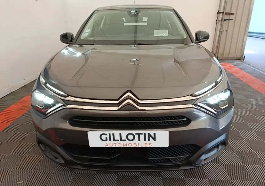 Vue avant d'une Citroën C4 gris clair avec feux LED allumés dans un showroom intérieur.