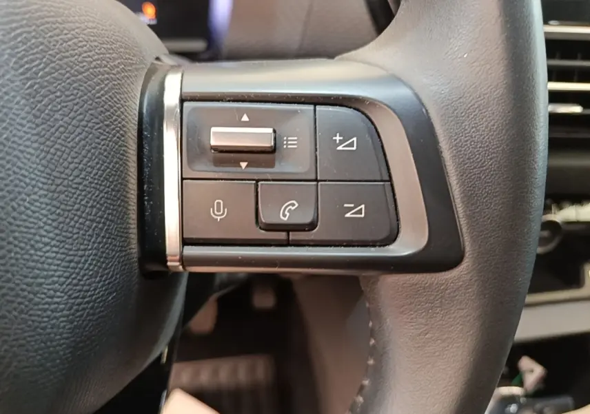 Gros plan sur les commandes multifonctions en cuir du volant côté gauche d'une Citroën C4 gris clair.