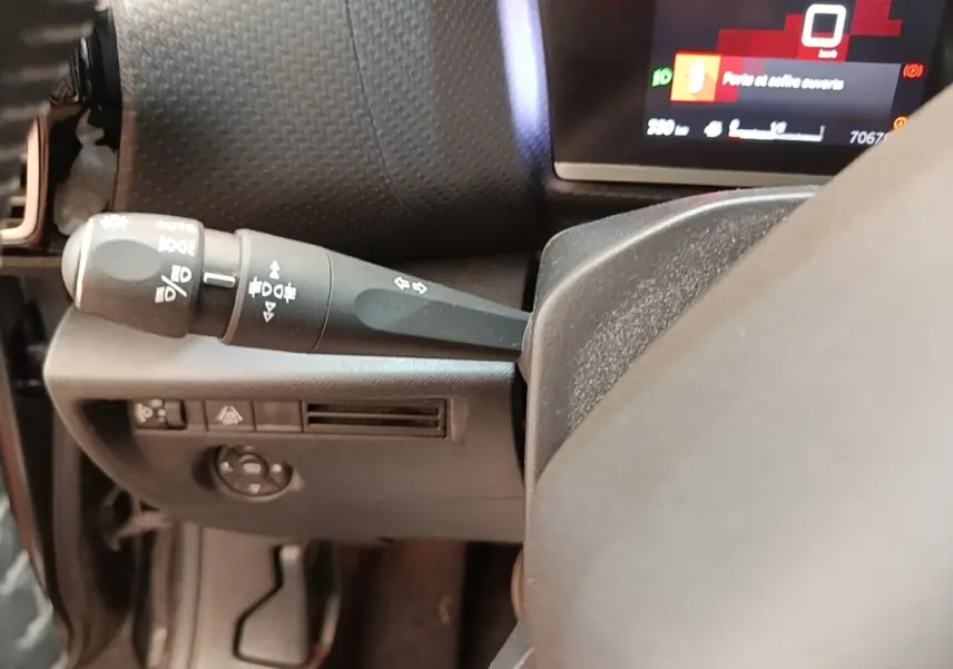 Détail du commodo gauche et partie du volant cuir dans l'habitacle d'une Citroën C4 gris clair, tableau de bord partiellement visible.