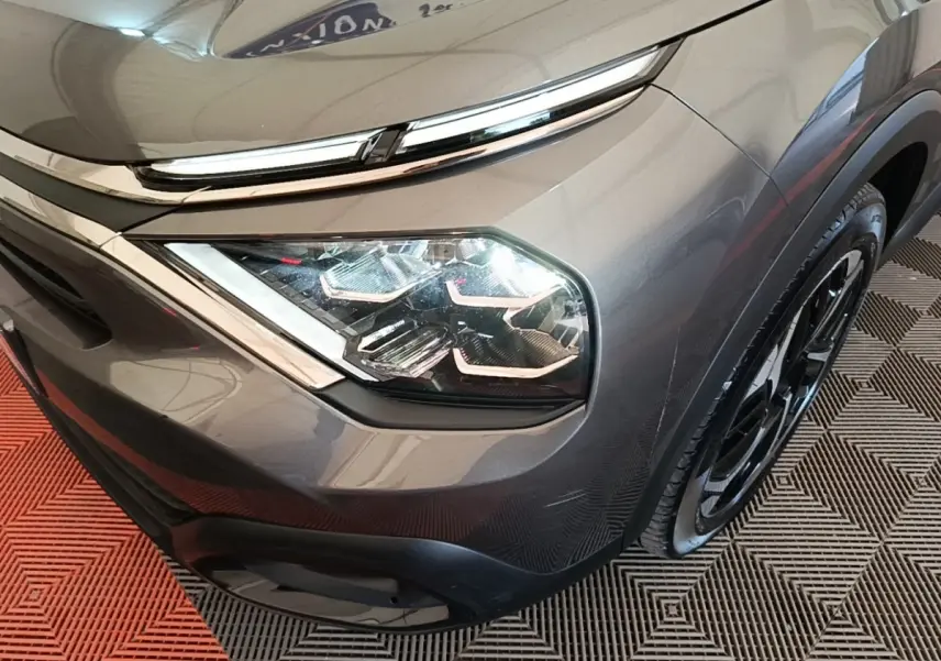 Gros plan sur le phare avant droit et la calandre d'une Citroën C4 gris clair, avec jante noire visible.
