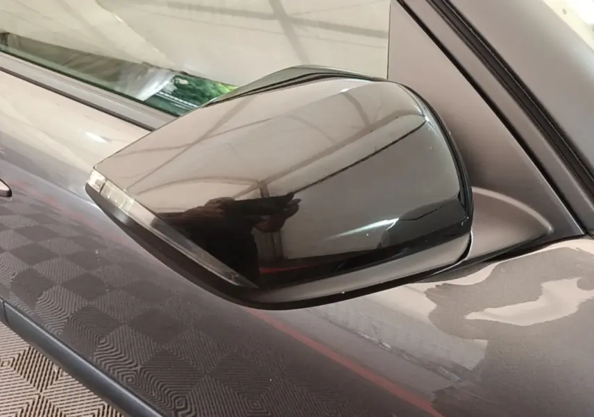 Rétroviseur droit noir brillant sur Citroën C4 gris clair, vue rapprochée avec reflet de l'environnement.