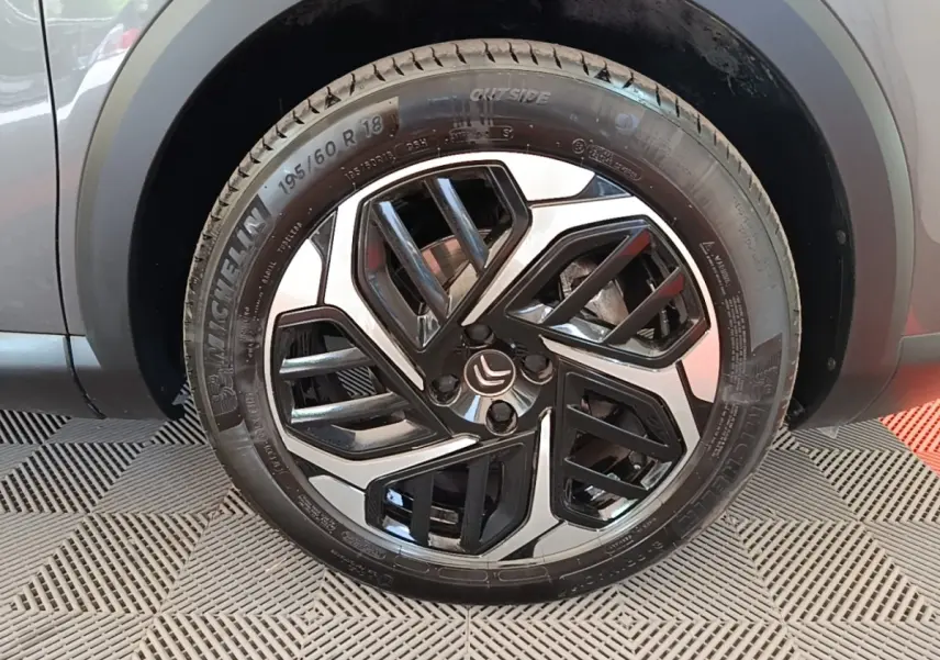 Gros plan sur la roue avant droite d’une Citroën C4 gris clair, avec jante alliage noire et argentée au design géométrique.