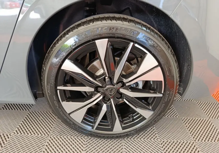 Gros plan sur la roue avant droite d'une Peugeot 308 gris foncé, jante alliage noir et argentée au design moderne.