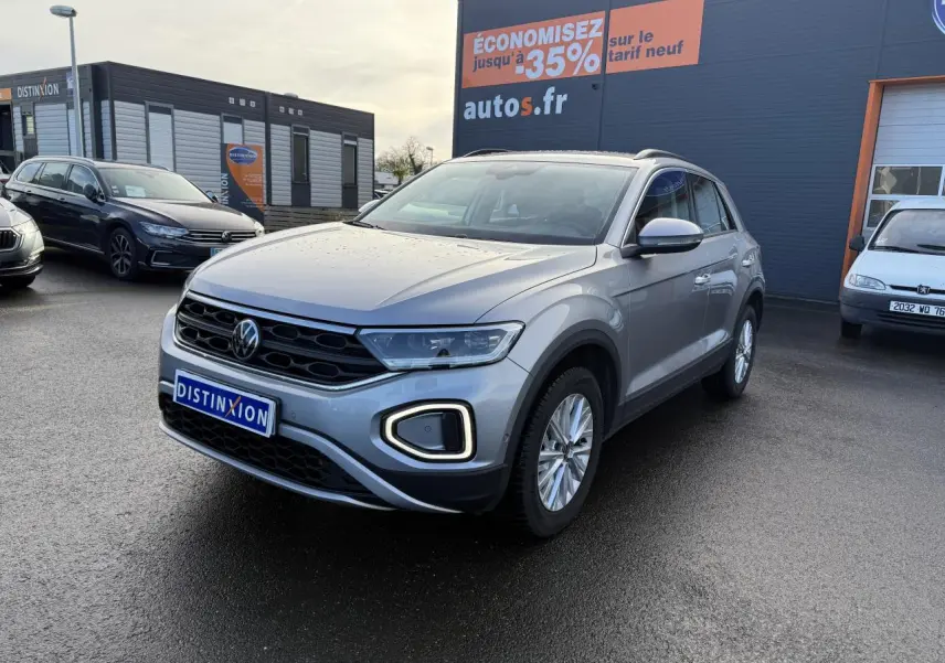Volkswagen T-Roc gris pyrite vu en 3/4 avant droit sur parking devant un bâtiment commercial autos.fr