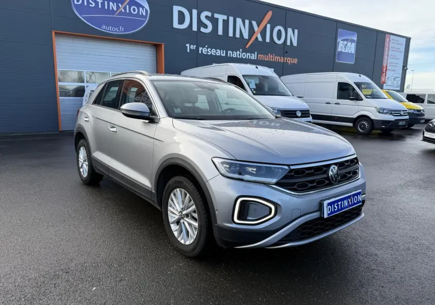 Volkswagen T-Roc gris pyrite en 3/4 avant droit, avec feux LED et calandre noire sur parking extérieur.