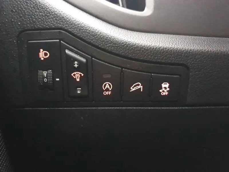 Gros plan sur les commandes noires du tableau de bord gauche du Kia Sportage blanc 2013, avec voyants orange allumés.