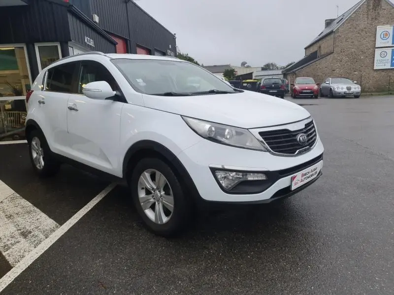 KIA SPORTAGE blanc vue 3/4 avant droit avec calandre chromée et jantes alliage sur parking humide