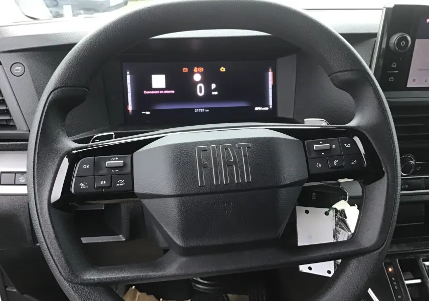 Vue rapprochée du volant noir du Fiat Scudo Fourgon 2024 avec tableau de bord numérique et commandes intégrées.