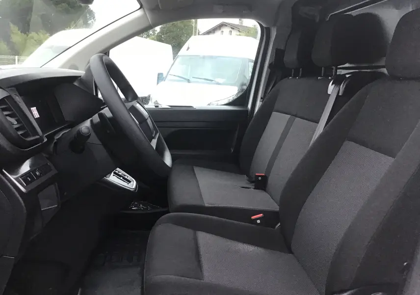 Vue intérieure côté conducteur du Fiat Scudo Fourgon 2024, sièges tissu gris et tableau de bord noir avec volant.