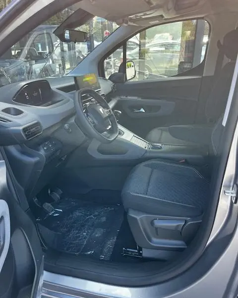 Intérieur avant droit du Peugeot Rifter gris foncé 2024, volant multifonctions, tableau de bord digital et siège tissu noir.