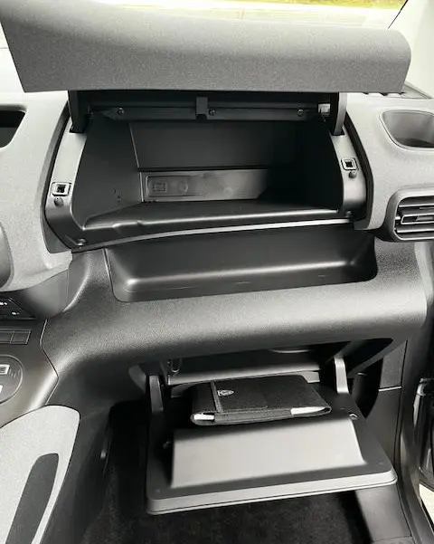 Vue intérieure du tableau de bord du Peugeot Rifter 2024 gris foncé, avec boîte à gants ouverte et rangement supérieur visible.