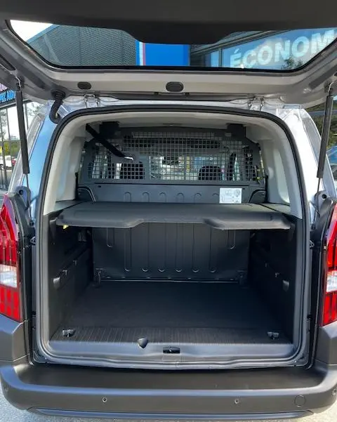 Vue arrière ouverte du Peugeot Rifter gris foncé 2024, montrant le coffre spacieux avec séparation métallique et tablette de rangement.