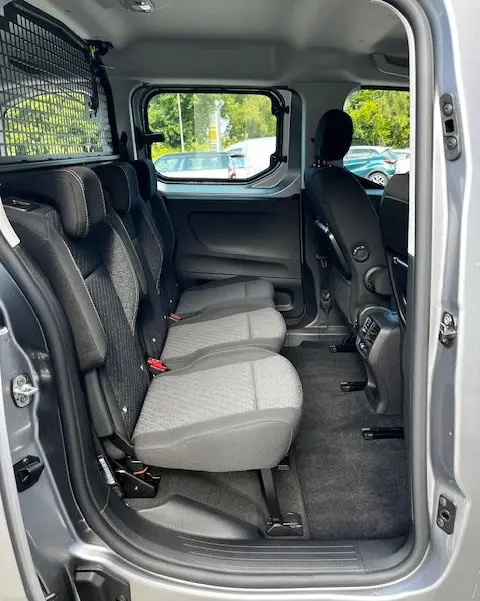 Vue intérieure côté droit des sièges arrière gris clair du Peugeot Rifter 1.5 BlueHDi 2024 avec séparation grillagée et fenêtre latérale.