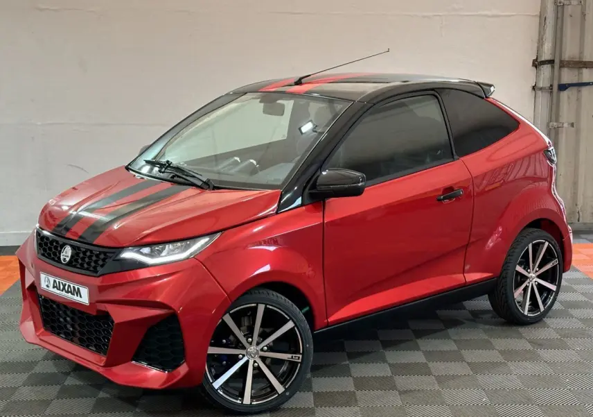Vue 3/4 avant droit d'une Aixam Ambition rouge 2026 avec bandes noires sur le capot et jantes alliage noires.