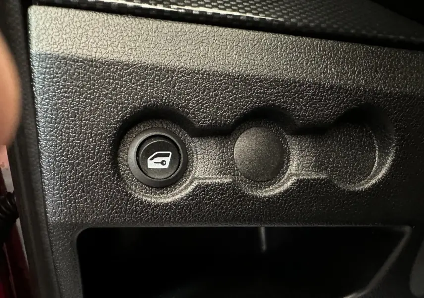 Bouton de déverrouillage du coffre sur tableau de bord noir texturé d'une Aixam Ambition rouge, vue intérieure rapprochée.