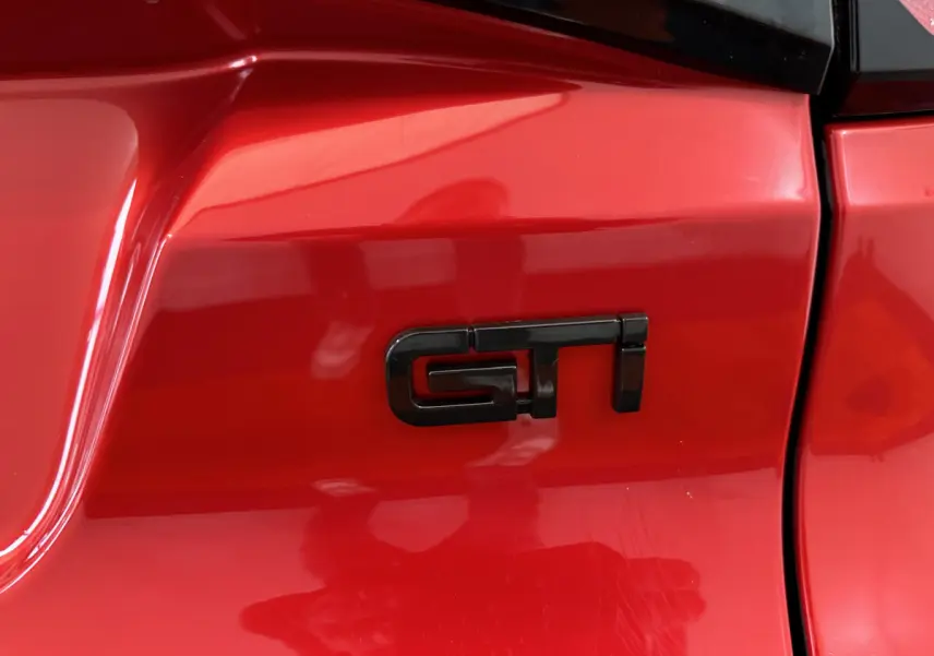 Gros plan sur l’inscription noire GTI sur la carrosserie rouge brillante d’une Aixam Ambition 0.5 City Coupe GTI.