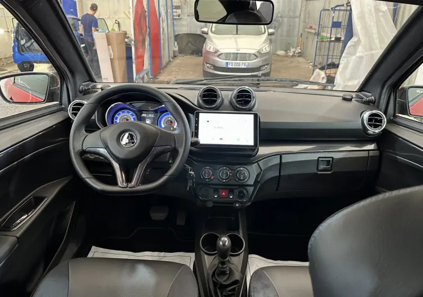 Vue intérieure de face du tableau de bord de l'AIXAM Ambition rouge, avec volant, écran tactile et commandes visibles.