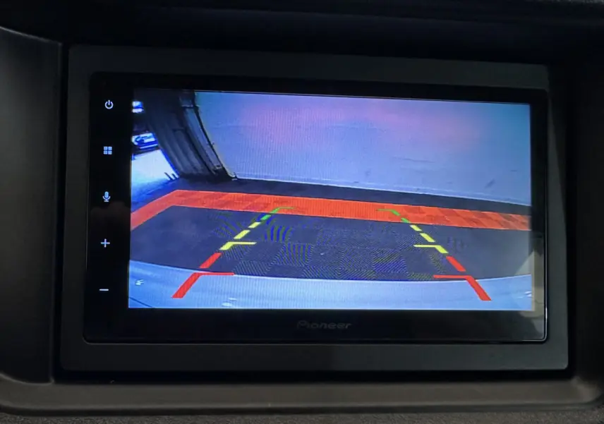 Écran intérieur montrant la caméra de recul avec repères colorés, dans une Aixam Ambition rouge 2026 côté conducteur.