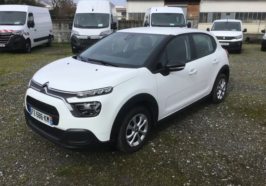 Citroën C3 blanche vue 3/4 avant droit, avec toit noir contrastant et jantes alliage, stationnée sur un sol gravillonné.