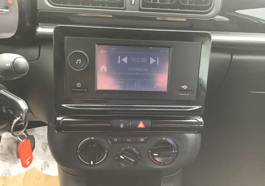 Vue rapprochée de la console centrale noire de la Citroën C3 blanche, avec écran tactile et commandes manuelles de climatisation.