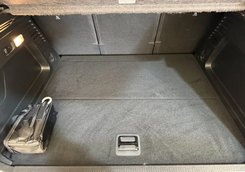 Coffre vu de face d'un Citroën C5 Aircross Hybrid bleu, avec tapis noir et un sac plié à gauche.