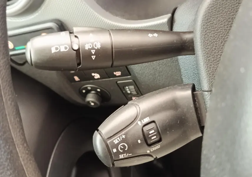Gros plan sur les commandes au volant du Peugeot Partner blanc, montrant les leviers de clignotants et régulateur de vitesse.
