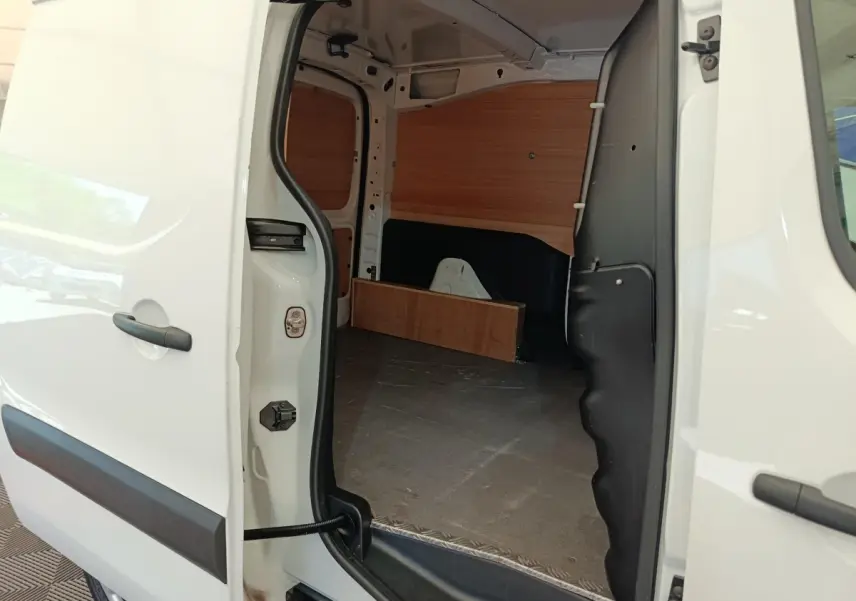 Vue intérieure depuis la porte latérale ouverte du Peugeot Partner blanc, montrant l’espace de chargement avec cloison bois.