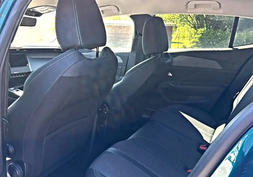 Vue intérieure arrière côté gauche du Peugeot 408 Hybrid bleu, montrant les sièges arrière et dossiers avant en tissu noir.