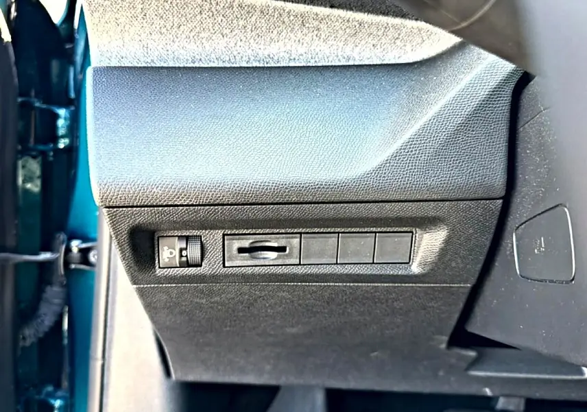 Vue rapprochée du tableau de bord côté gauche d’une Peugeot 408 bleu 2025, avec commandes de réglage des phares.