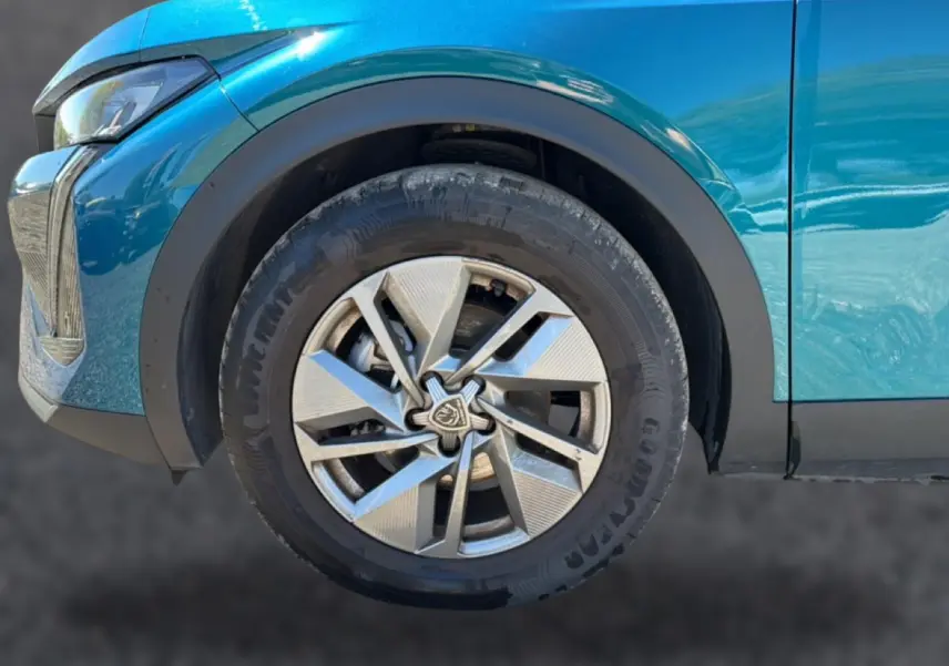 Gros plan sur la roue avant gauche d'une Peugeot 408 Hybrid 145 allure e-dcs6 bleu, avec jante alu et logo Peugeot central.