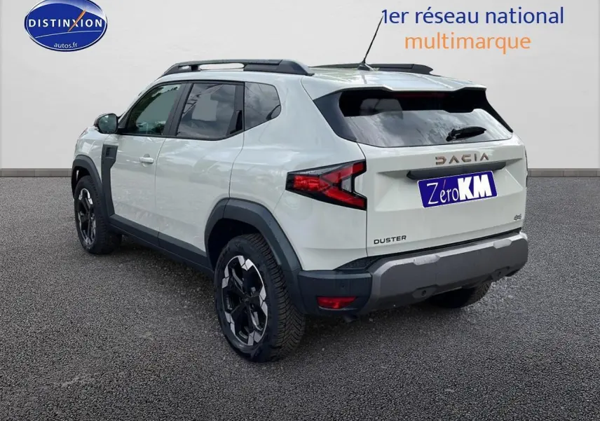 Vue 3/4 arrière droite d'un Dacia Duster 2025 couleur Sandstone avec barres de toit et jantes noires.