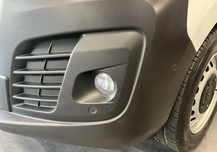 Gros plan sur le pare-chocs avant droit noir avec antibrouillard et roue acier du Citroën Jumpy blanc.
