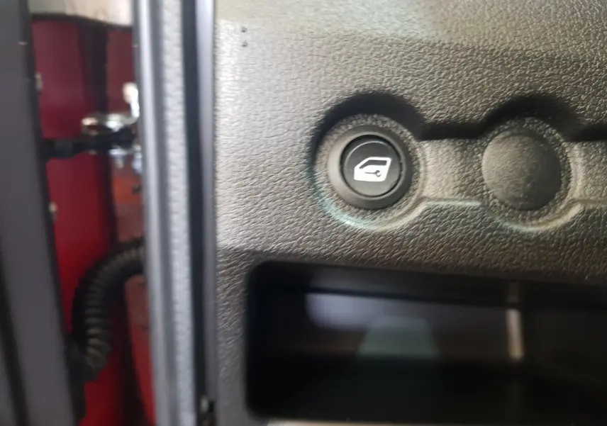 Bouton d'ouverture de coffre sur panneau intérieur noir d'une Aixam Ambition 0.5 City Pack rouge, vue rapprochée.