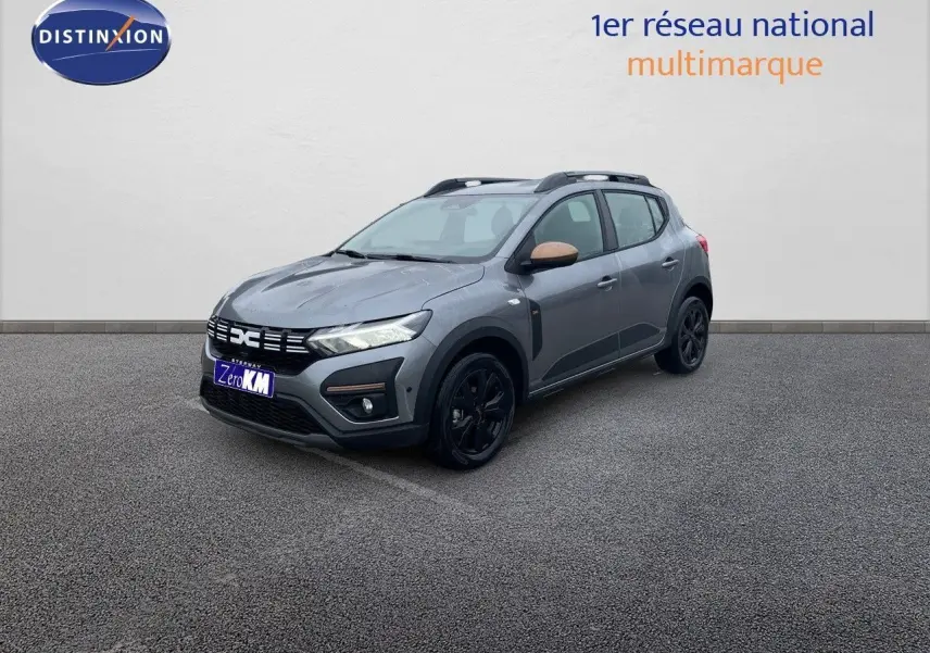Vue 3/4 avant droite d'une Dacia Sandero Stepway 2024 gris schiste métal avec rétroviseurs bronze et jantes noires.