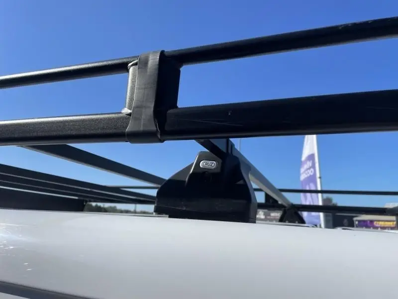 Détail du système de barres de toit noires CRUZ sur le toit blanc d'un Peugeot Expert Fourgon 2023, vue rapprochée.