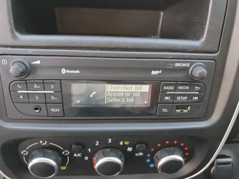 Vue rapprochée de la console centrale du Renault Trafic Fourgon blanc, mettant en valeur l'autoradio Bluetooth et les commandes de climatisation.