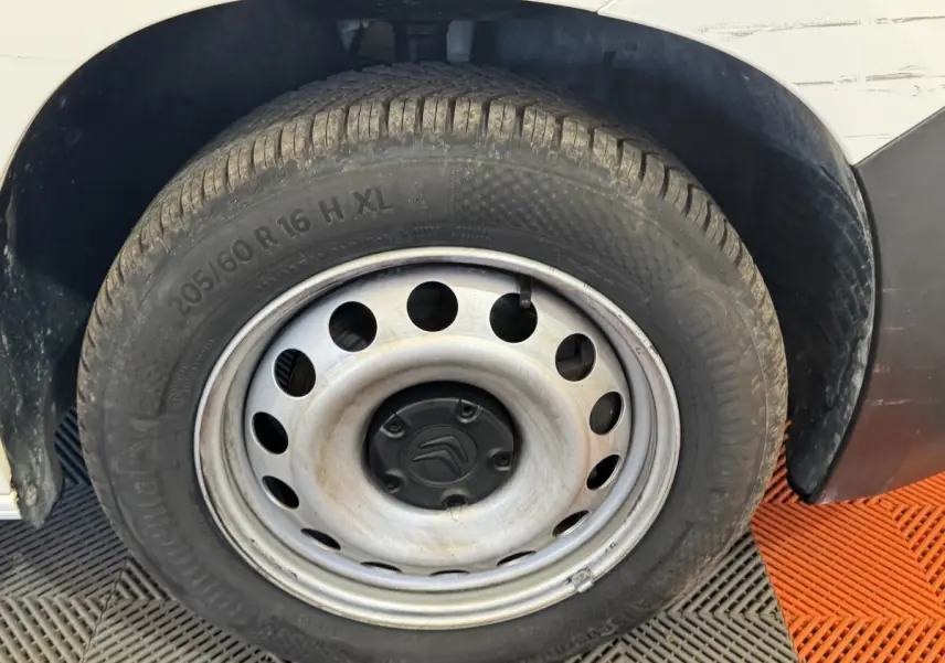 Gros plan sur la roue avant droite d’un Citroën Berlingo blanc avec jante acier et logo Citroën au centre.