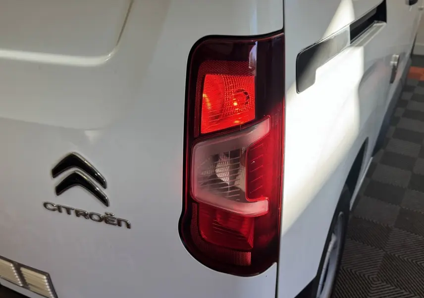 Gros plan sur le feu arrière droit d’un Citroën Berlingo blanc, avec logo et poignée de porte visibles.