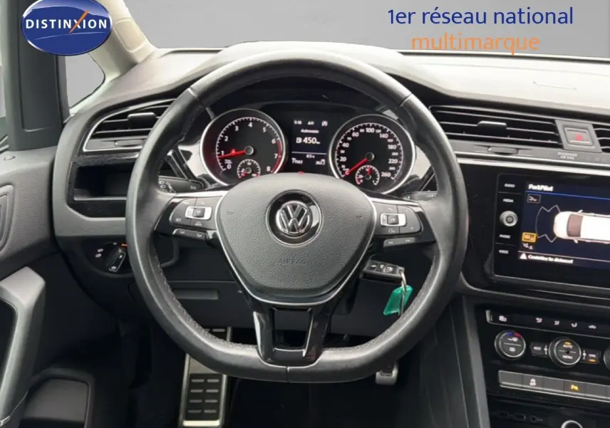 Vue intérieure centrée sur le volant de la Volkswagen Touran 2018 avec tableau de bord et écran tactile visibles.