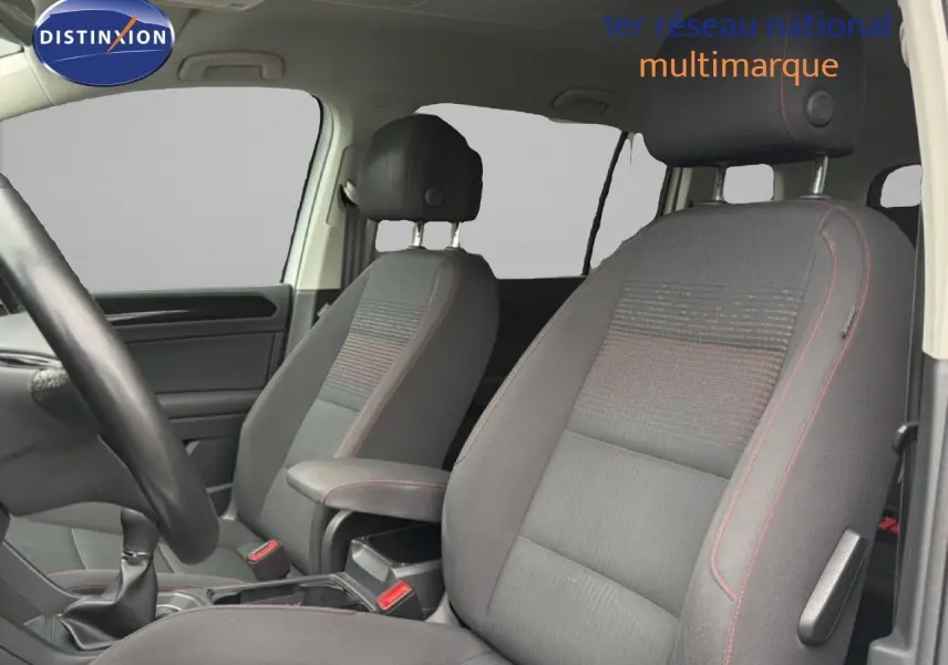 Vue intérieure côté conducteur du Volkswagen Touran blanc de 2018, montrant les sièges avant en tissu gris avec surpiqûres rouges.