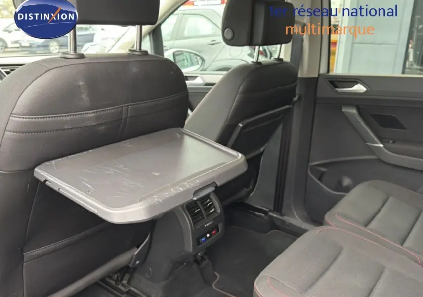 Vue intérieure arrière droite du Volkswagen Touran blanc, mettant en valeur la tablette rabattable et les sièges en tissu gris.