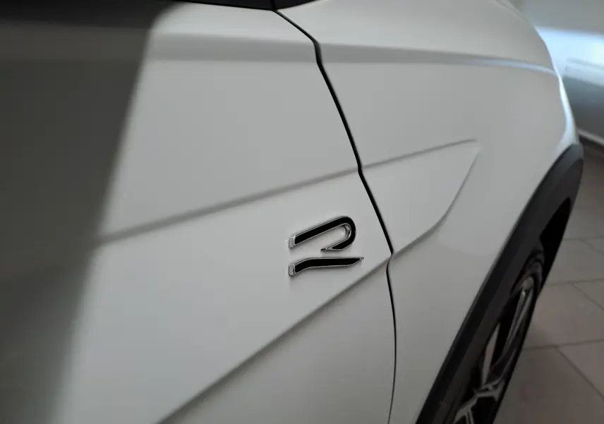 Gros plan sur l'aile avant droite blanche du Volkswagen Taigo 2025 avec logo R-Line et jante alliage visible.