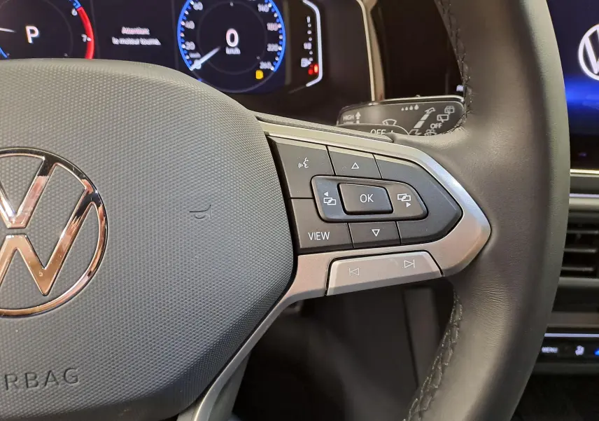 Gros plan sur le volant multifonction du Volkswagen Taigo 2025, avec commandes et logo VW visibles.
