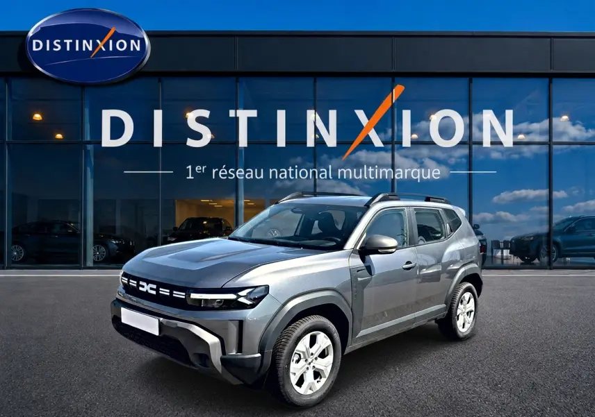 Dacia Duster 1.2 hybrid-g 150 gris schiste en 3/4 avant droit, avec barres de toit et jantes alu visibles.
