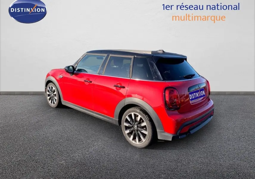 Vue 3/4 arrière droite d'une MINI 1.5 136CH rouge chili à toit noir, avec jantes noires et cinq portes visibles.
