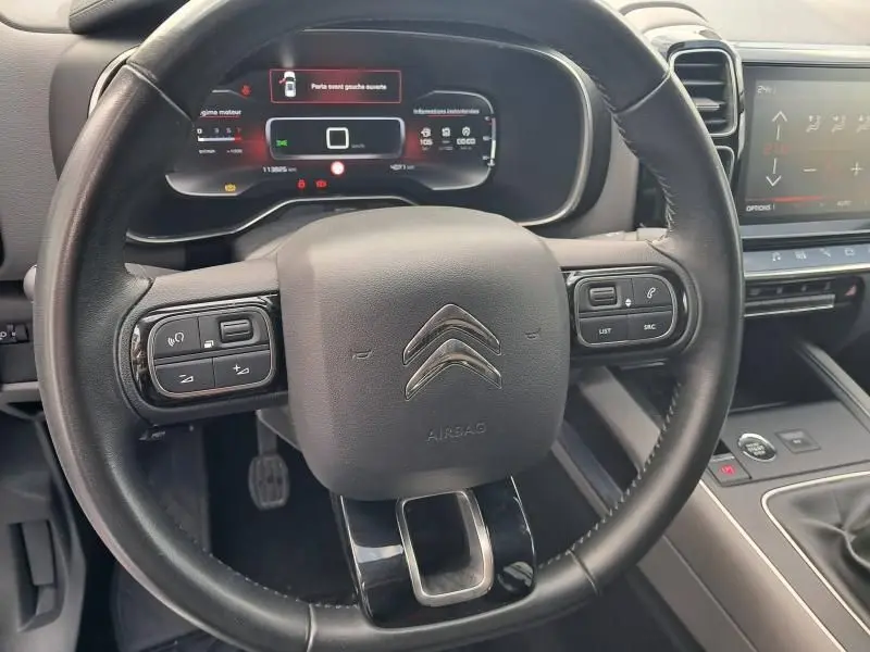 Vue rapprochée du volant cuir noir du Citroën C5 Aircross HDi 130 Shine 2019 avec tableau de bord numérique allumé.