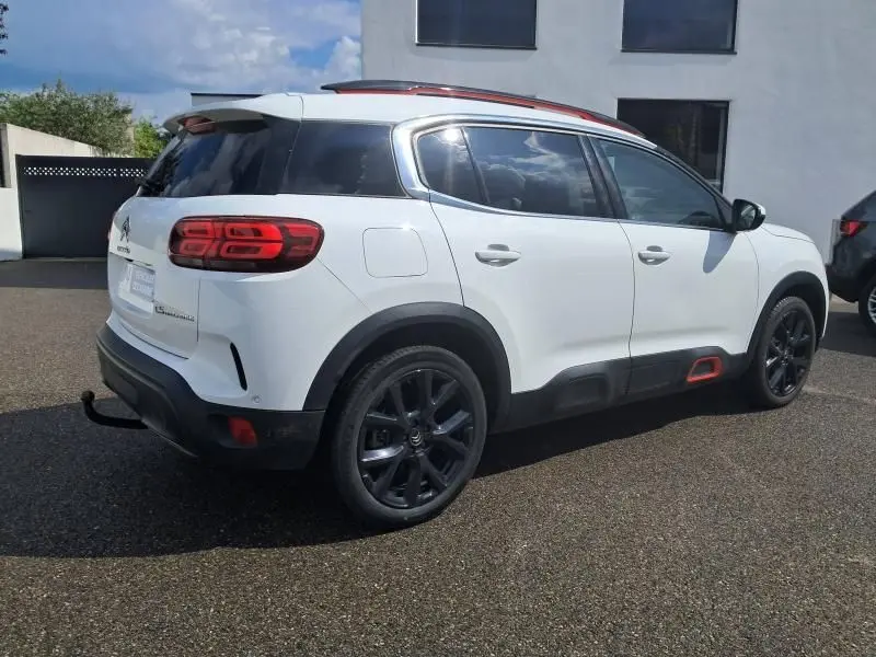 Vue 3/4 arrière droite d'un Citroën C5 Aircross blanc 2019 avec jantes noires et détails rouges sur les bas de caisse.