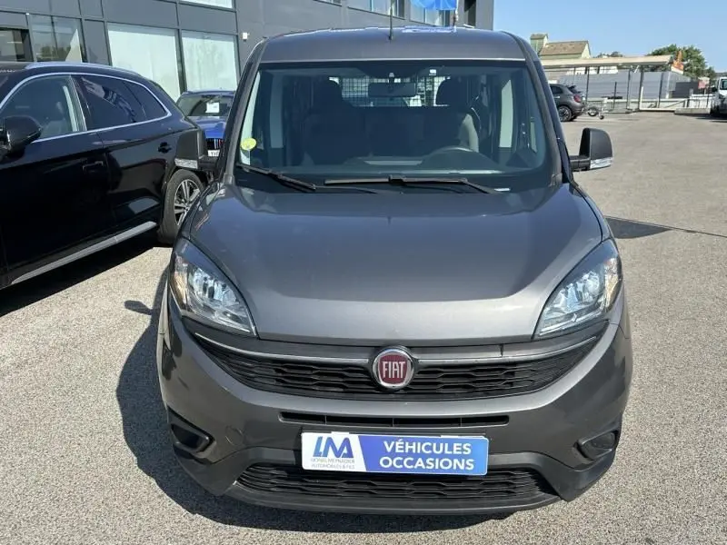 Vue frontale d'un FIAT Doblo Cargo gris foncé avec calandre noire et plaque "Véhicules Occasions" visible.