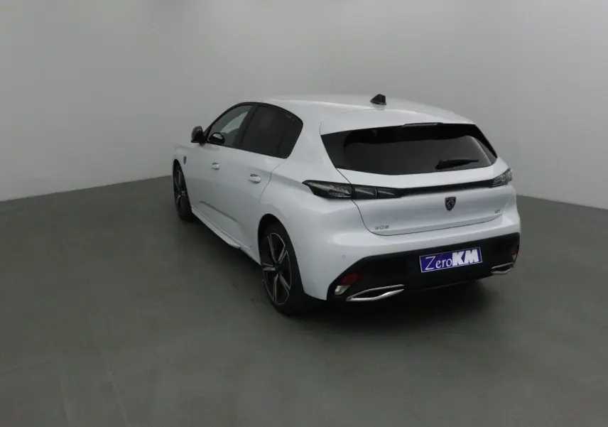 Vue 3/4 arrière droite d'une Peugeot 308 blanche Okenite, avec jantes alliage et vitres teintées dans un studio gris.