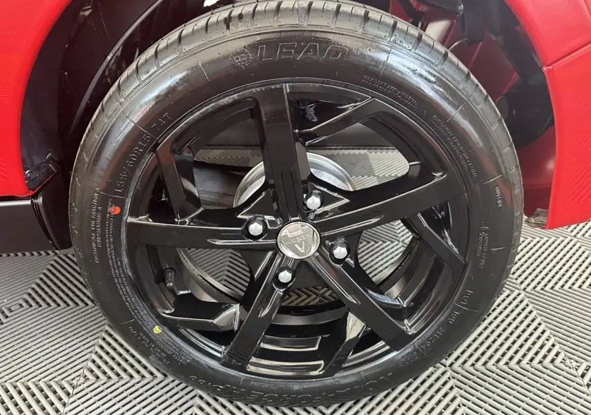 Gros plan sur la roue avant droite noire brillante d'une Aixam Ambition 0.5 City Sport rouge, avec jante cinq branches.